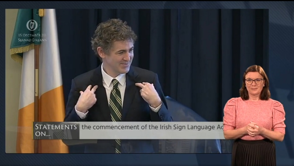 Video still of the Dáil Chamber with the Chairperson signing and an ISL interpreter in the foreground